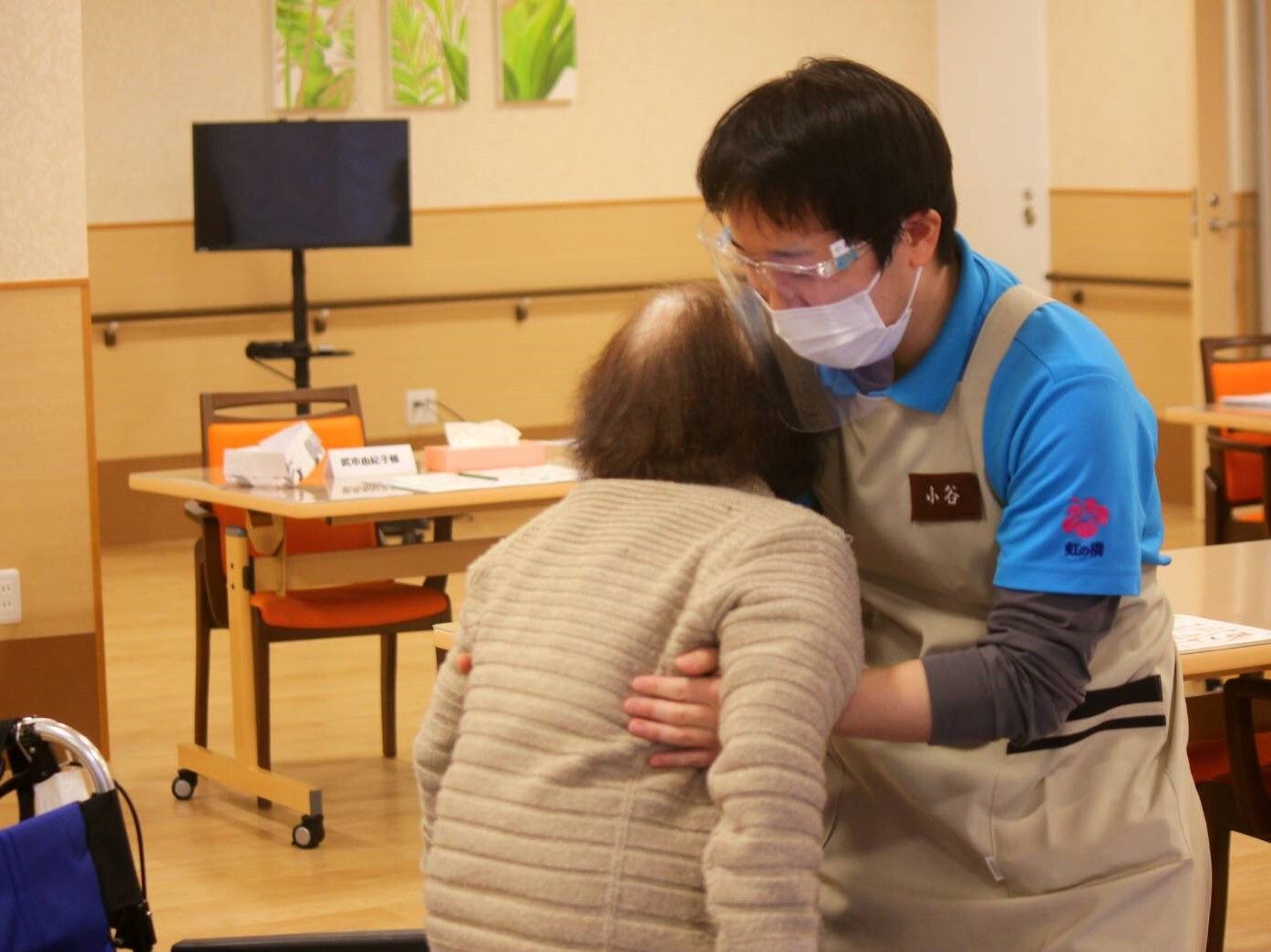 笑顔でこちらを向いている施設のスタッフと車いすに乗っている高齢者の様子。施設で写された写真