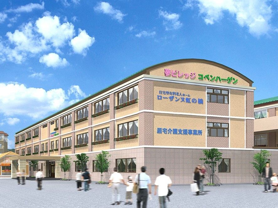 ３階建ての建物はベージュ系で建物の周りには木が植えられている。家族連れなどたくさんの人が歩いている。