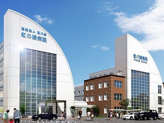 白衣を着た女性スタッフが車いすの高齢女性の車いすを押し移動している様子。二人とも笑顔。
