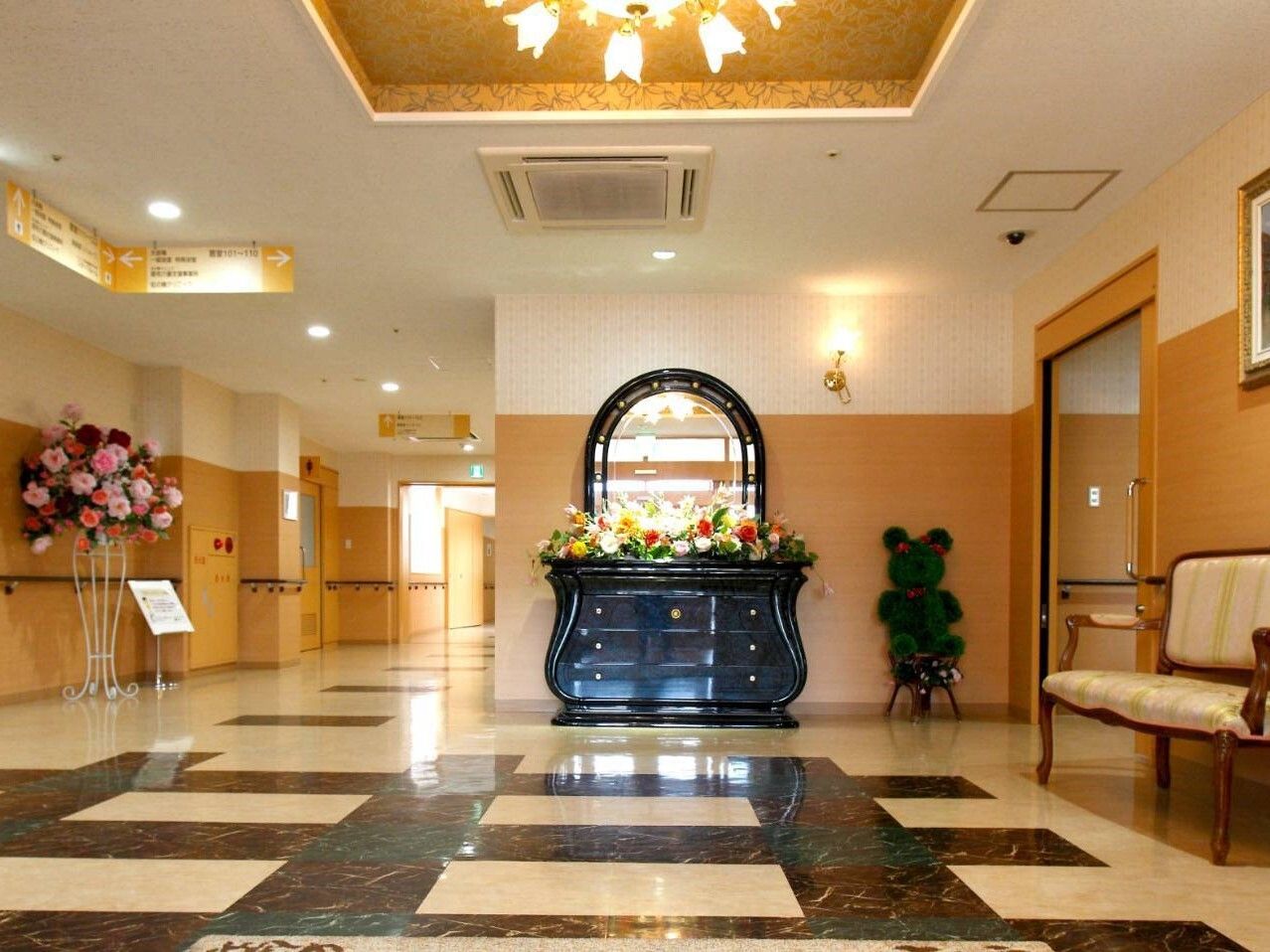 ３階建ての建物はベージュ系で外壁にはホーム名や併設事業所の名前が書かれている。周辺には多くの人が歩いている。