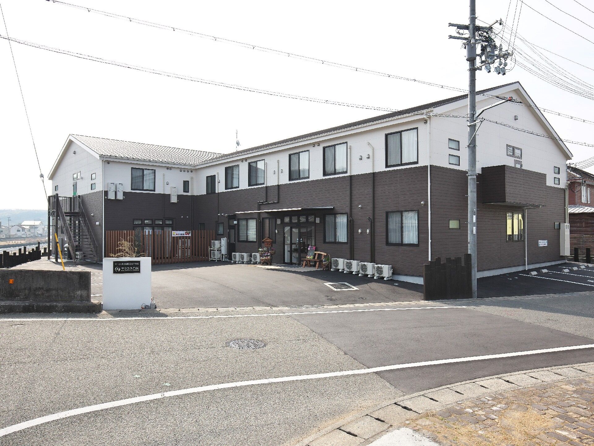 車いすの高齢女性が付き添いの高齢男性と若い男女のスタッフと一緒に屋外で笑っている。