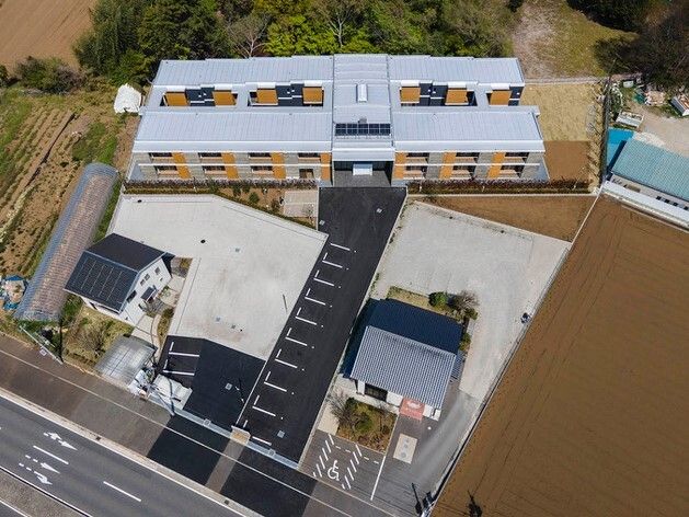 上空から住宅と周辺を見た様子。広い敷地内には駐車場があり、２件民家のような家も建っている。
