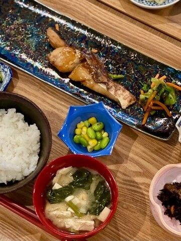 白いご飯のみそ汁、焼き鮭に枝豆、ヒジキの煮物などが並び、赤い箸も置かれている。