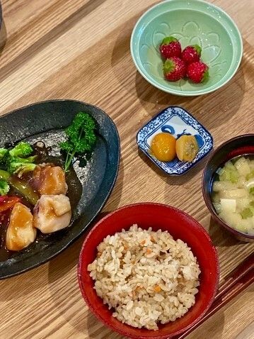 いちごやびわ、炊き込みご飯に味噌汁、鶏肉のソテーの野菜添えなどが並んだ木製のテーブル。