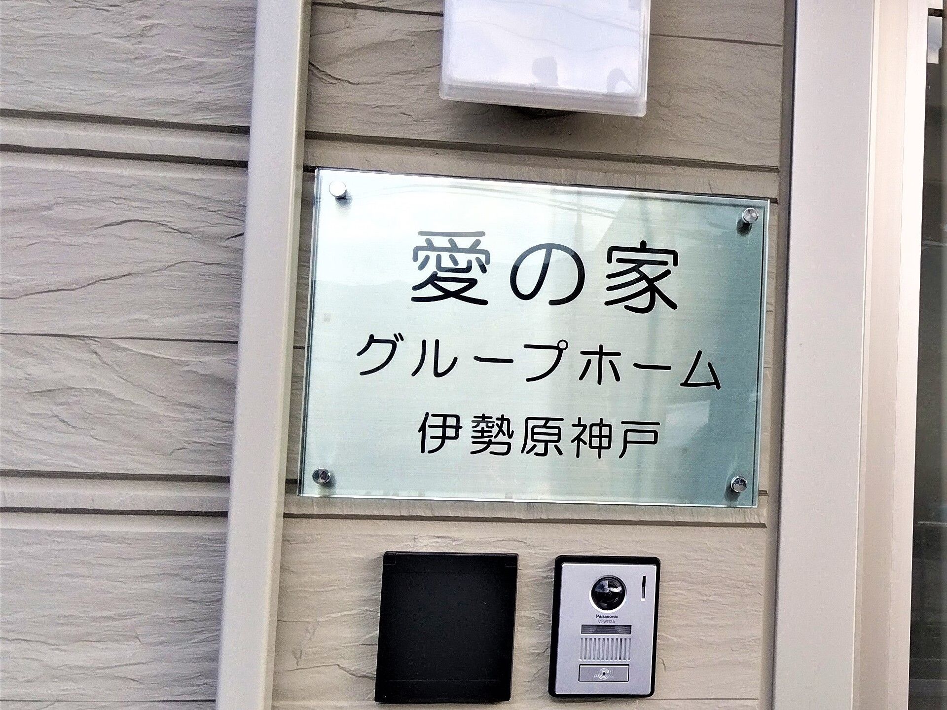 ブルーのエプロンを付けた若い女性スタッフと車いすの高齢女性が笑顔で屋外で過ごしている。