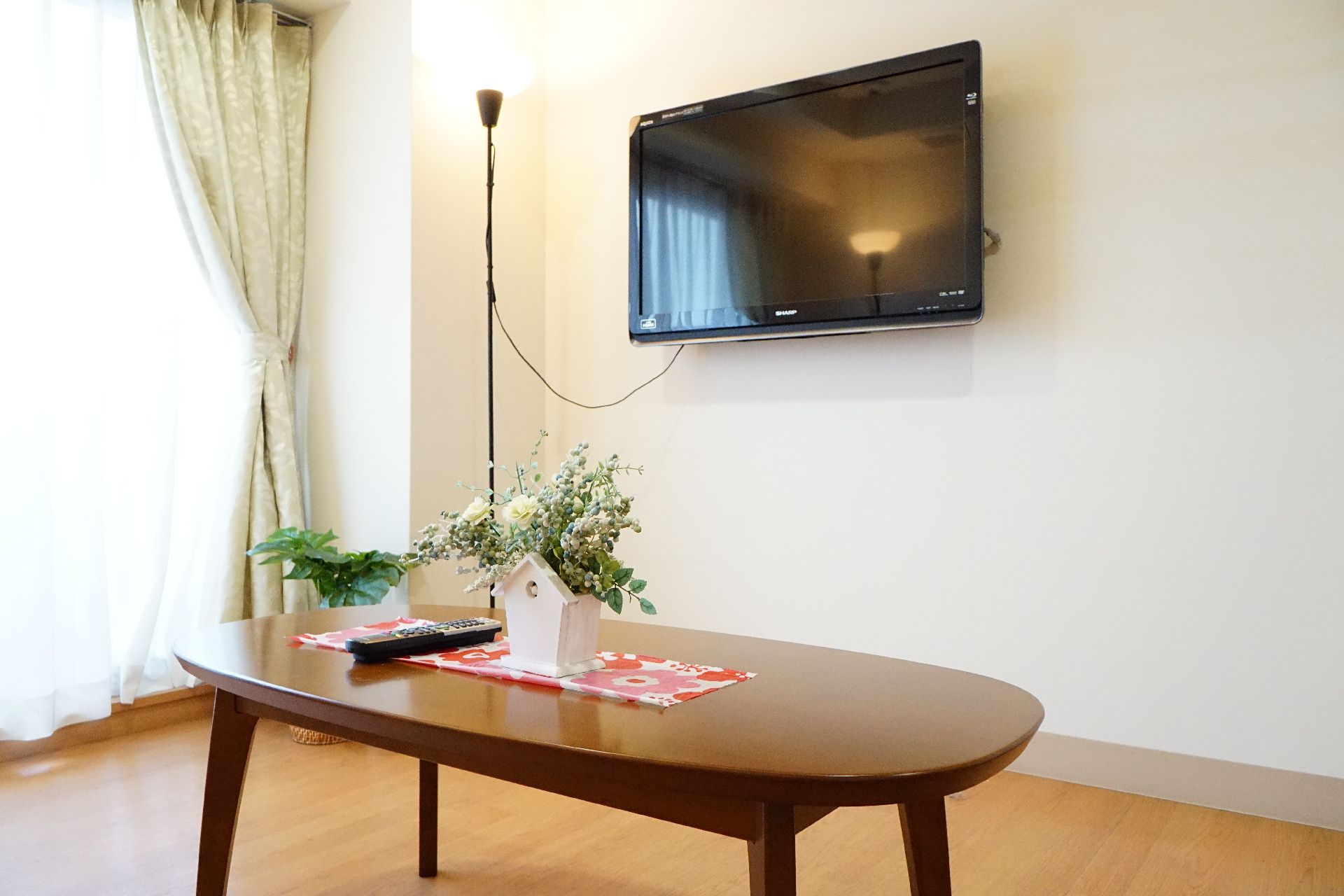 窓から光が差し込み、壁掛けのテレビとテーブルが設置されている居室