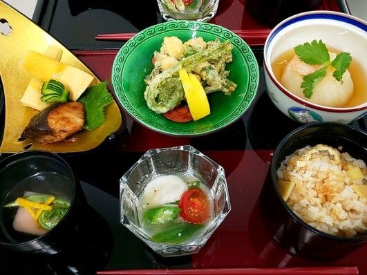 野菜の天ぷらやブリの照り焼き、トマトの和え物、炊き込みご飯、吸い物などが並んでいる。