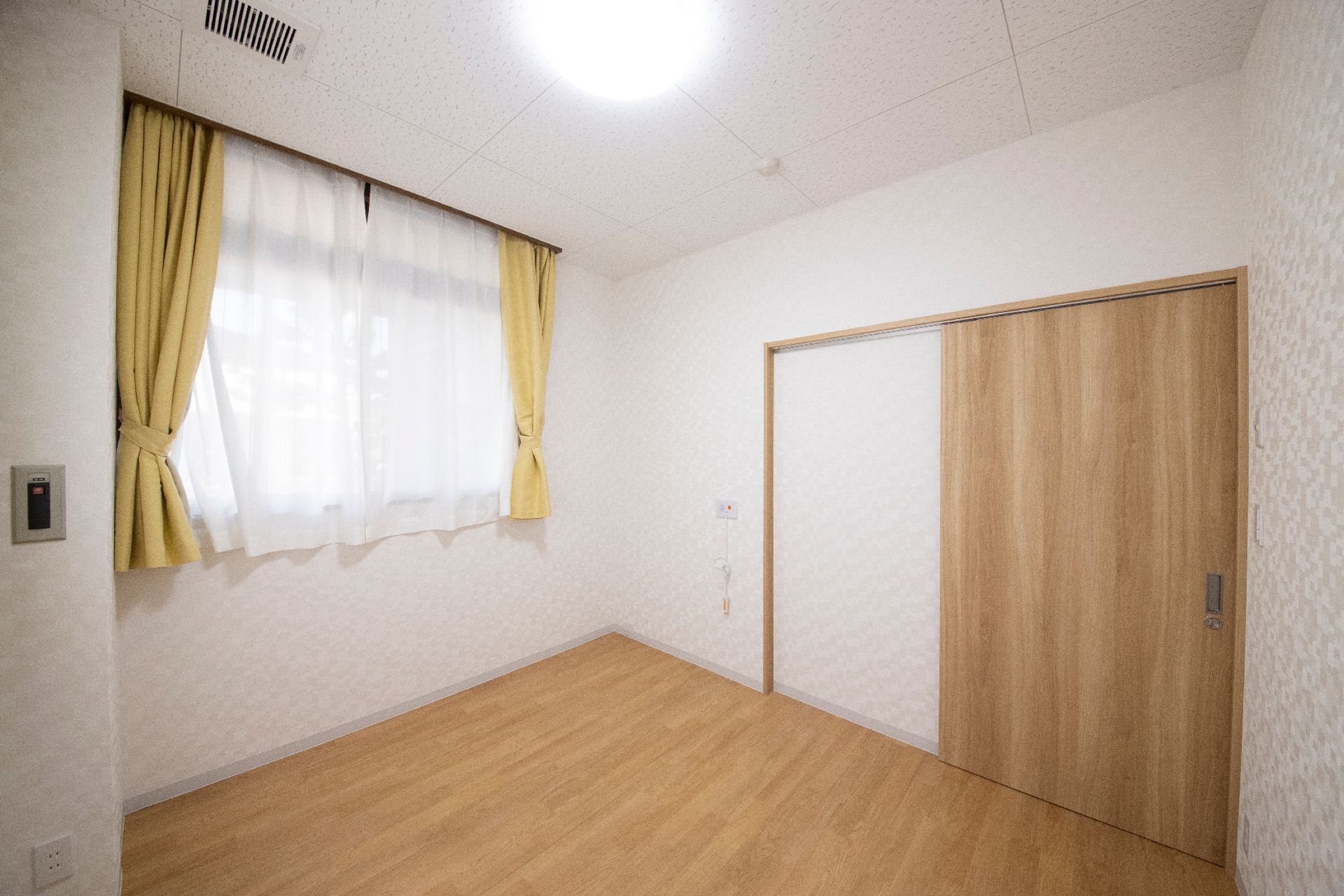 薬を飲もうとしている高齢女性のそばにはエプロンを付けた女性スタッフがいて、コップを持っている。