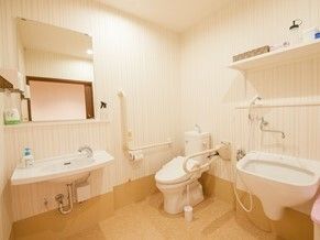 介助スペースが広いトイレには手すりが複数付き、オレンジの呼び出しボタンもあり、手洗い場もある。