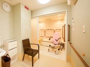 ブラウン系の手すりが付いた白を基調とした浴室。脱衣所にはいすが置かれ、呼び出しボタンが設置されている。