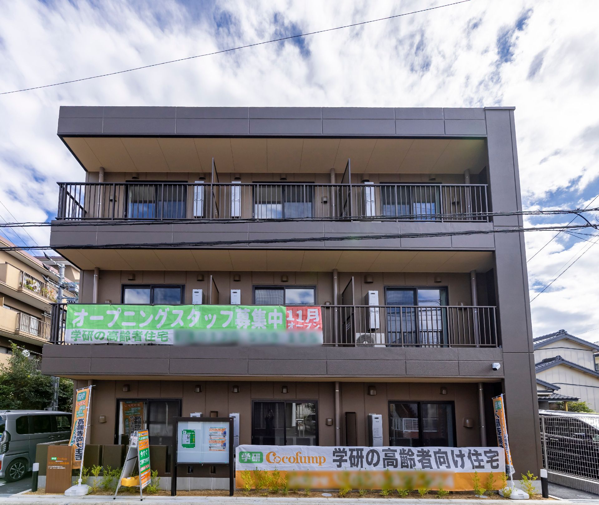 ３階の建物でベランダや玄関に広告の垂幕をしている外観