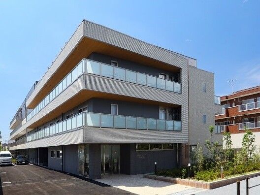 グレー系の外観の２階建ての建物は日当たり良好で敷地内には草木が植えられたスペースや駐車場もある。