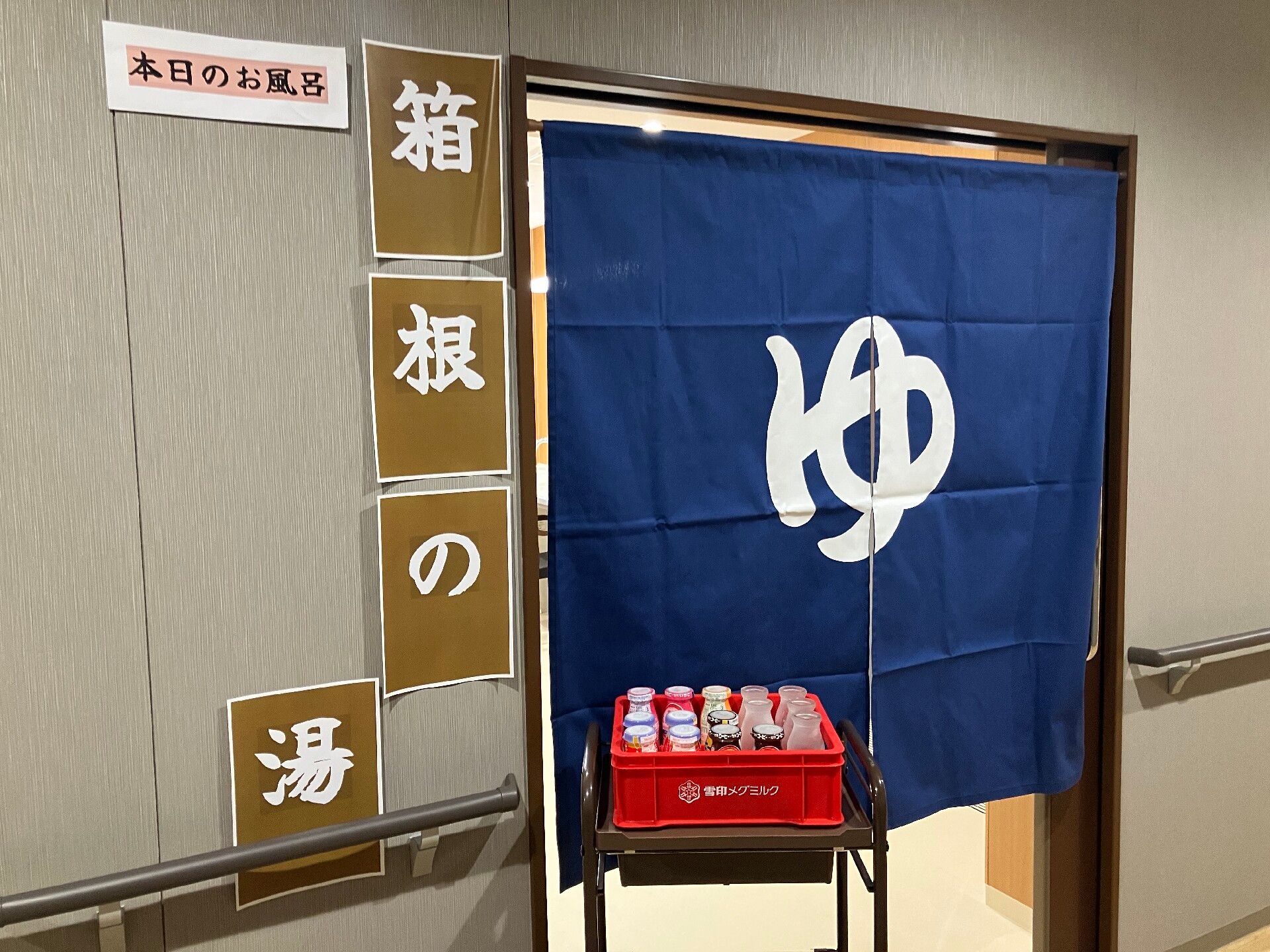 「箱根の湯」と書かれた紙が貼られている。浴室のドアには「ゆ」と書かれた暖簾がかかっている。