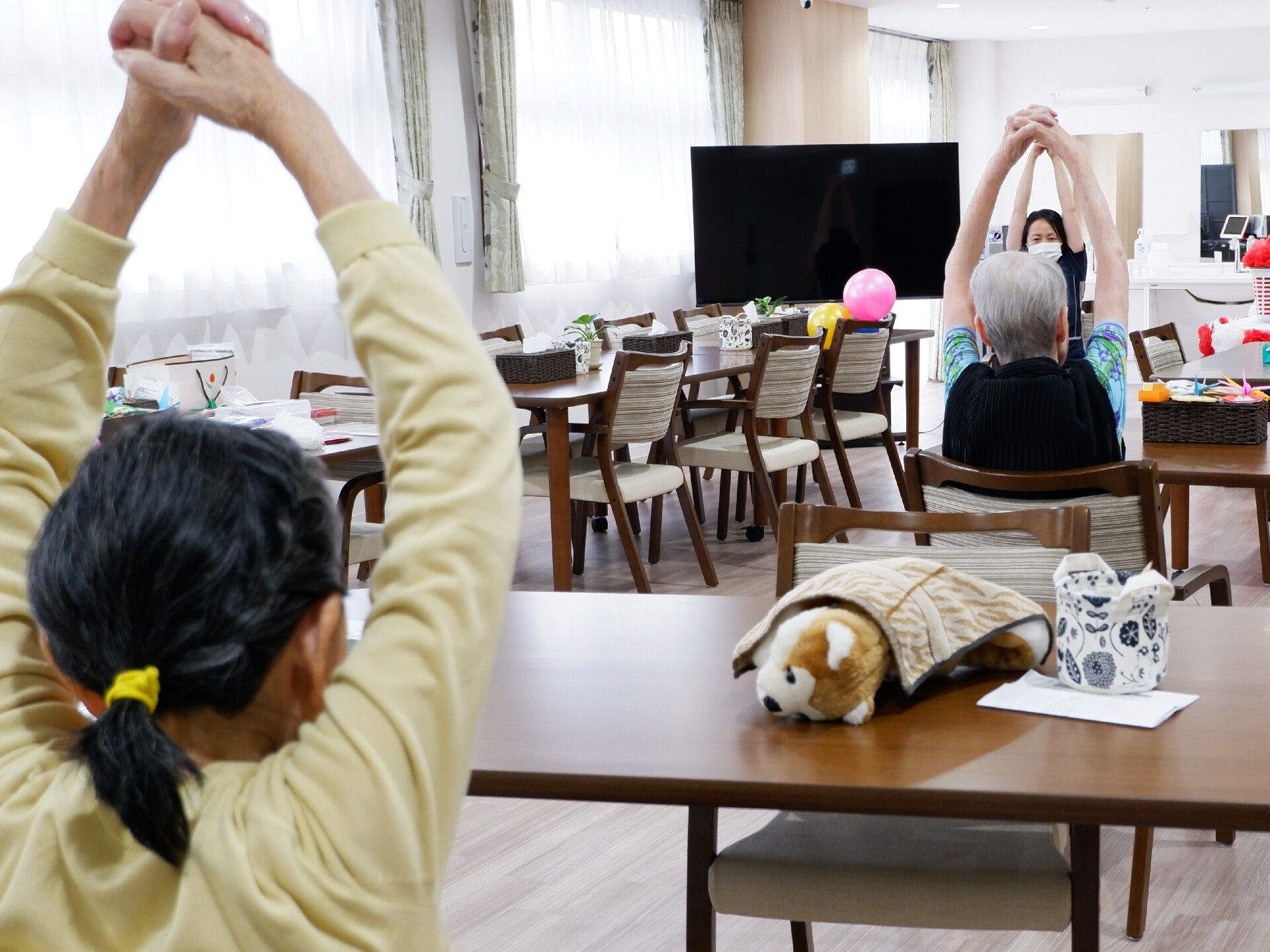 椅子に座ったまま両手を上げているスタッフに習ってエクササイズを行っている高齢者たち。
