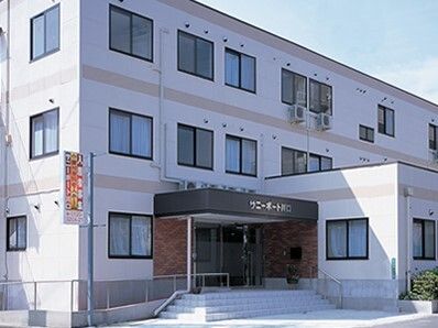 玄関に手すり付きの階段とスロープが設置されている３階建ての建物。玄関には屋根も付いている。