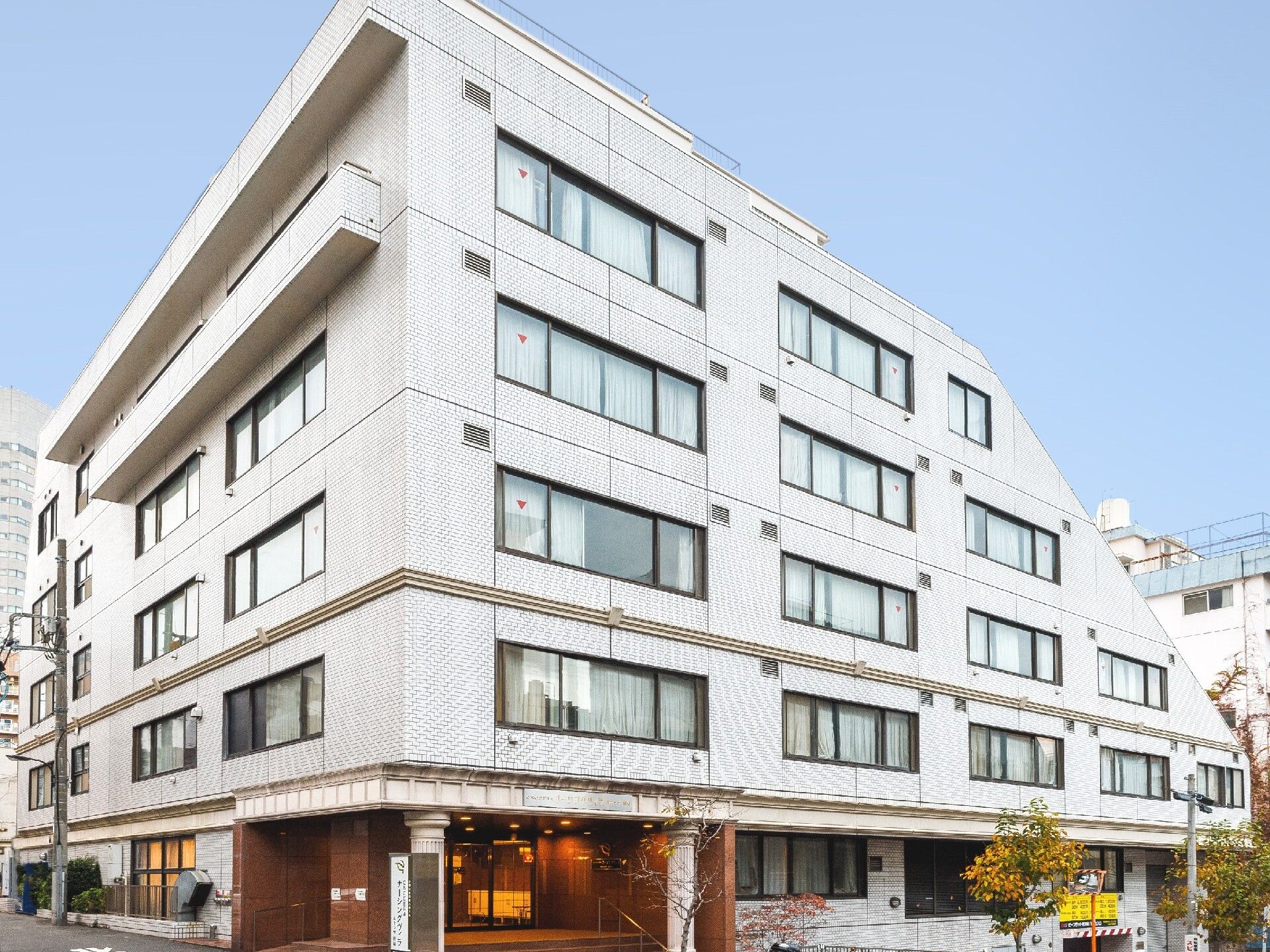 7階建ての建物は白を基調としていて日当たり良好。建物の周辺には草木も植えられている。
