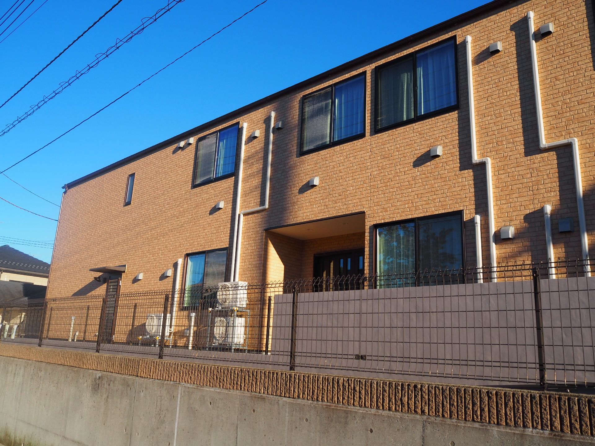 2階部分にはベランダが付いている２階建ての建物はベージュ系で日当たりのいい場所に建っている。