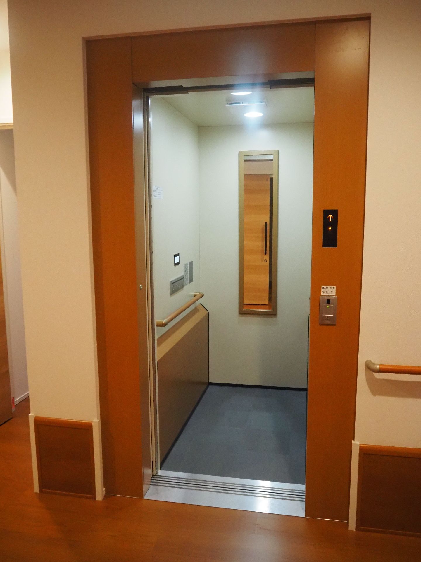 庫内に鏡や手すりが付いたエレベーター。扉の横には車いすやエレベーターのマークが貼られている。