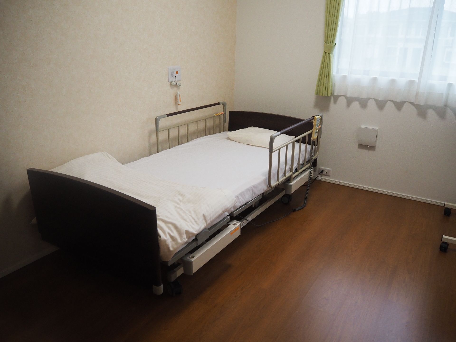 フローリングの部屋は寝具付きのベッドがあり、レースカーテンとカーテンが付いた窓が付いている。