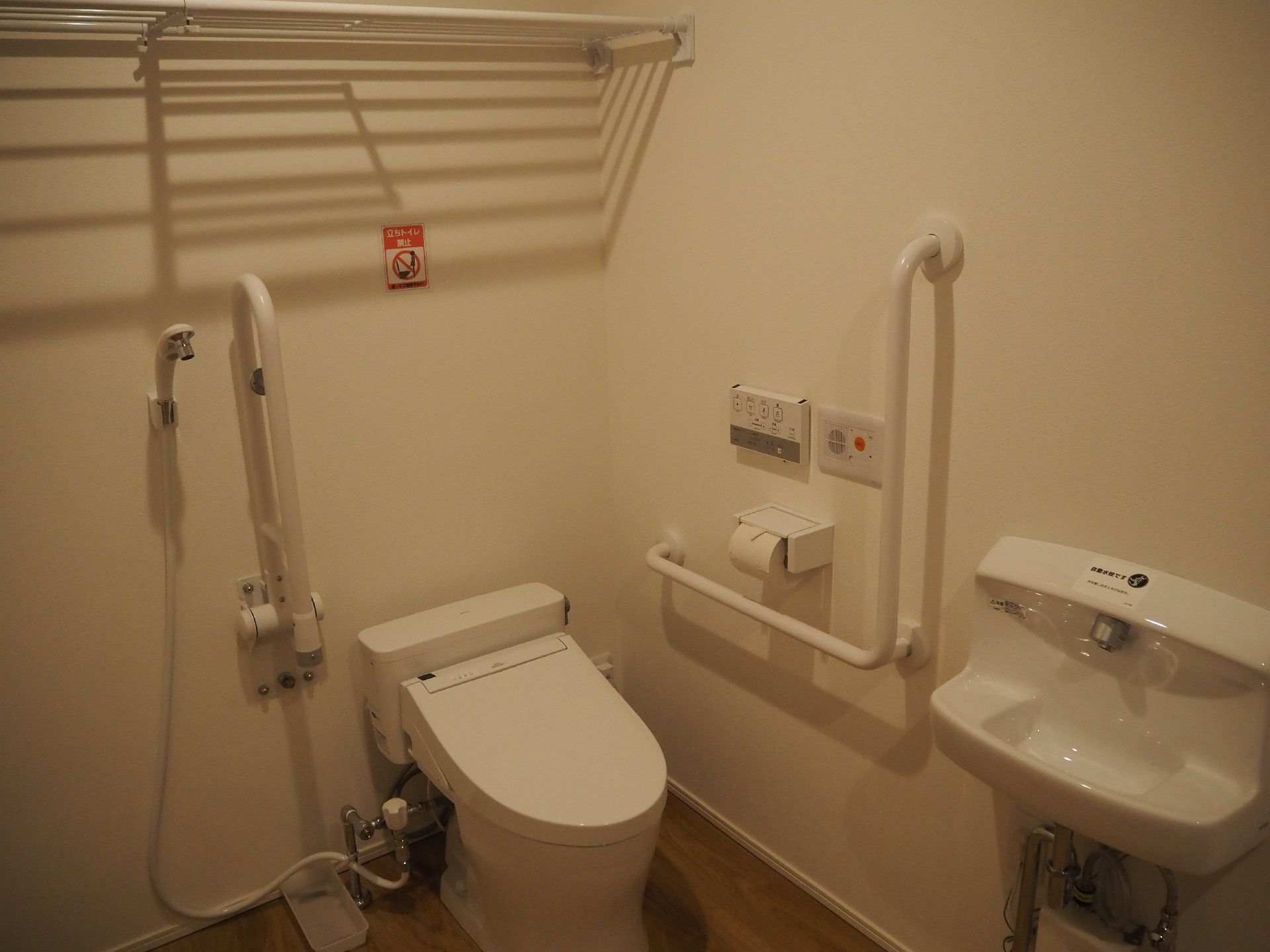 背もたれや手すりが付いたトイレ。トイレットペーパーホルダーの上にはオレンジの呼び出しボタンもある。