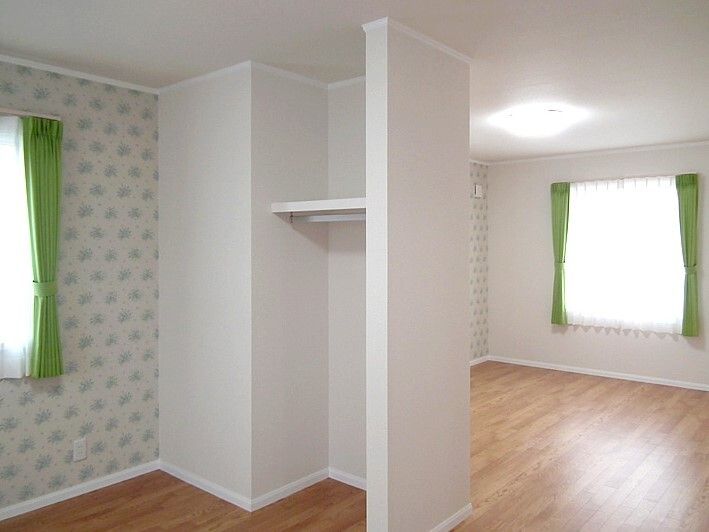 グリーンのカーテンが付いた窓があるフローリングの部屋にはオープンタイプの収納スペースがある。