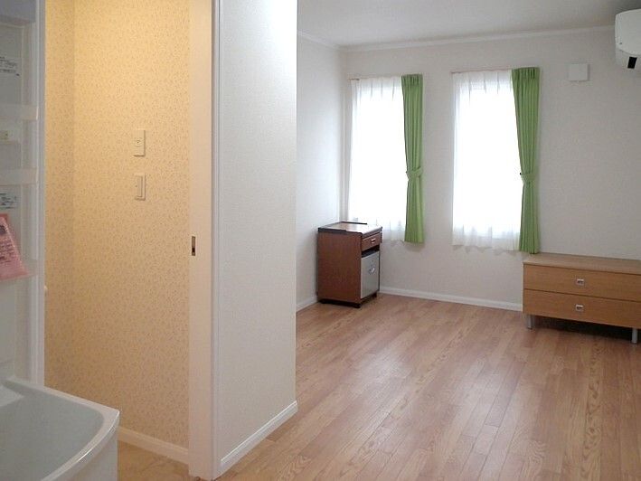 レースカーテンとカーテンが付いた窓があるフローリングの部屋にはエアコンもついている。