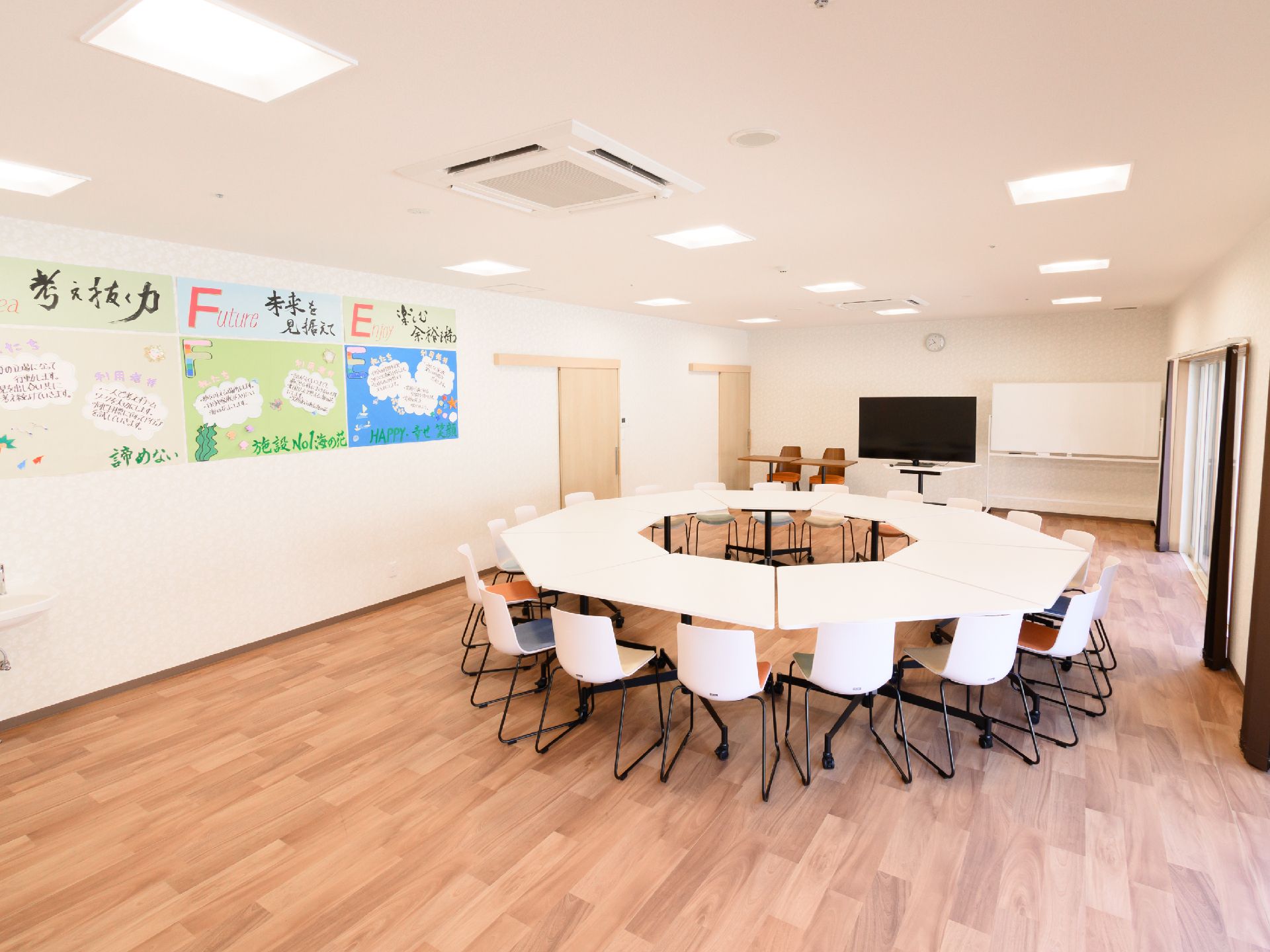 白い壁の窓がある部屋にきれいに並べられた白い机と白い椅子