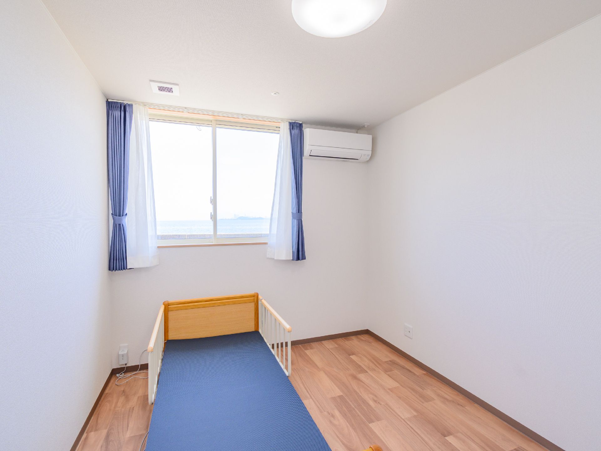 青いマットレスが敷かれたベッドが置かれた白い壁の部屋