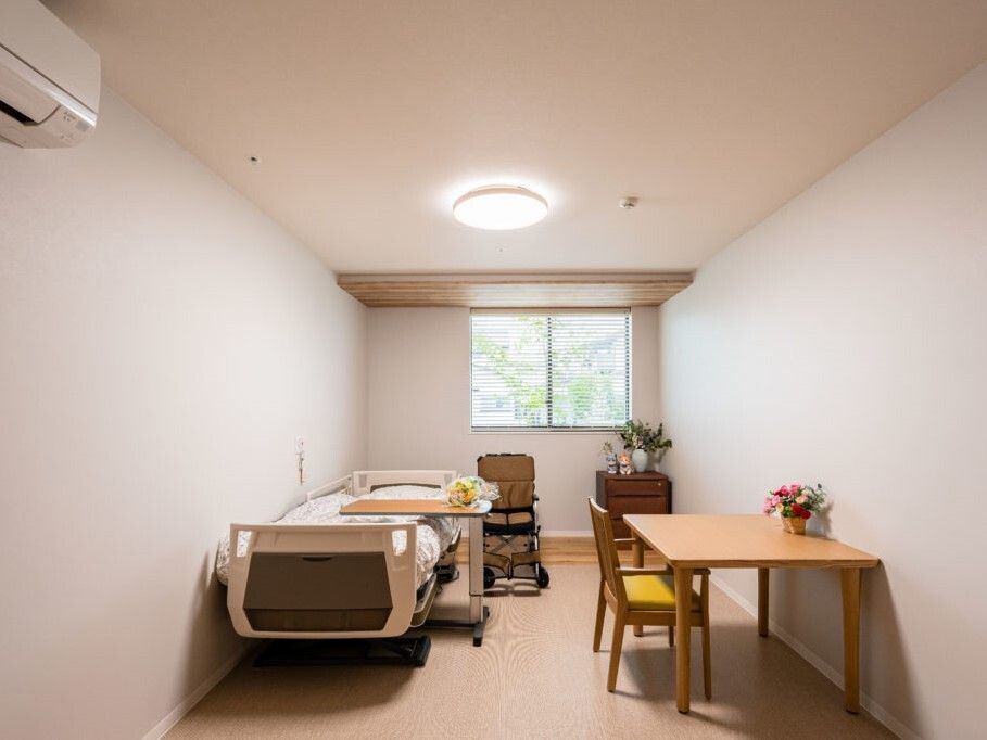 寝具付きのベッドやテーブルセットが置かれたフローリングの部屋には花や観葉植物が飾られている。