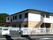 白とベージュの２階建ての建物。屋外階段が設置され、敷地内には駐車場があり、車が止まっている。