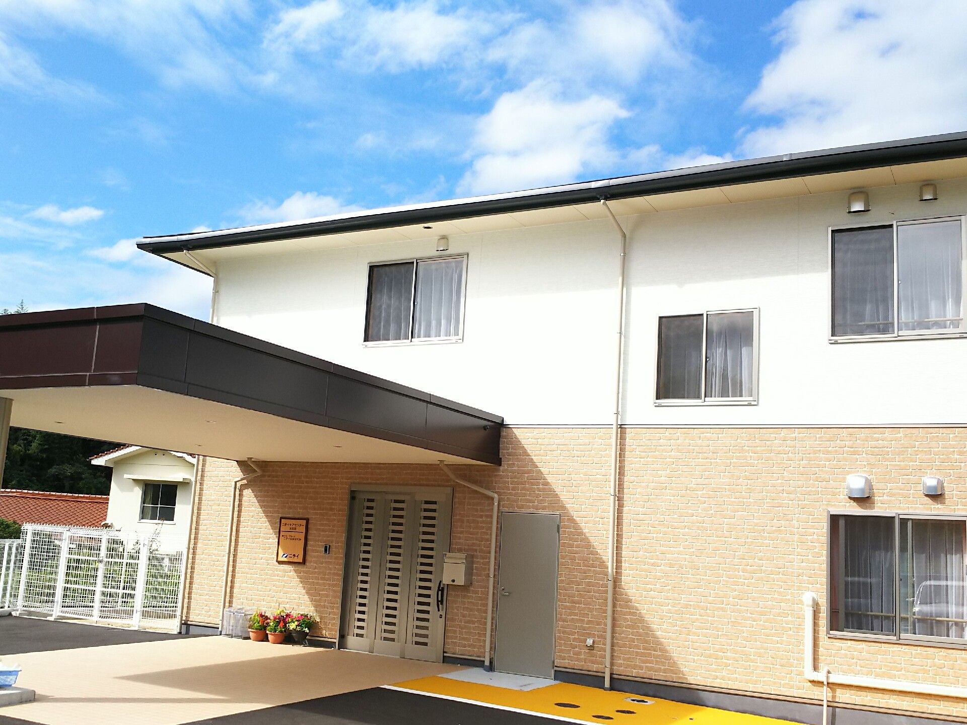 大きな車寄せが付き、日当たりのいい場所に建っている２階建ての建物。玄関先には花が飾られている。