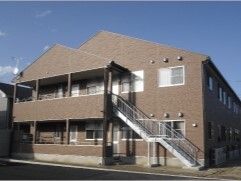 ２階建ての建物は日当たり良好でブラウン系の外壁。屋外階段も設置されている。