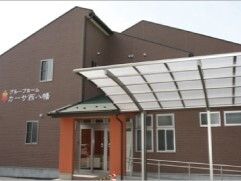 ブラウン系の外壁の2階建ての建物。建物の前にはカーポートがあり、外壁にはホーム名が書かれている。