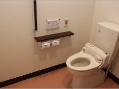 オレンジの呼び出しボタンや手すりが付いたトイレは介助スペースが広く、便座のふたはない。