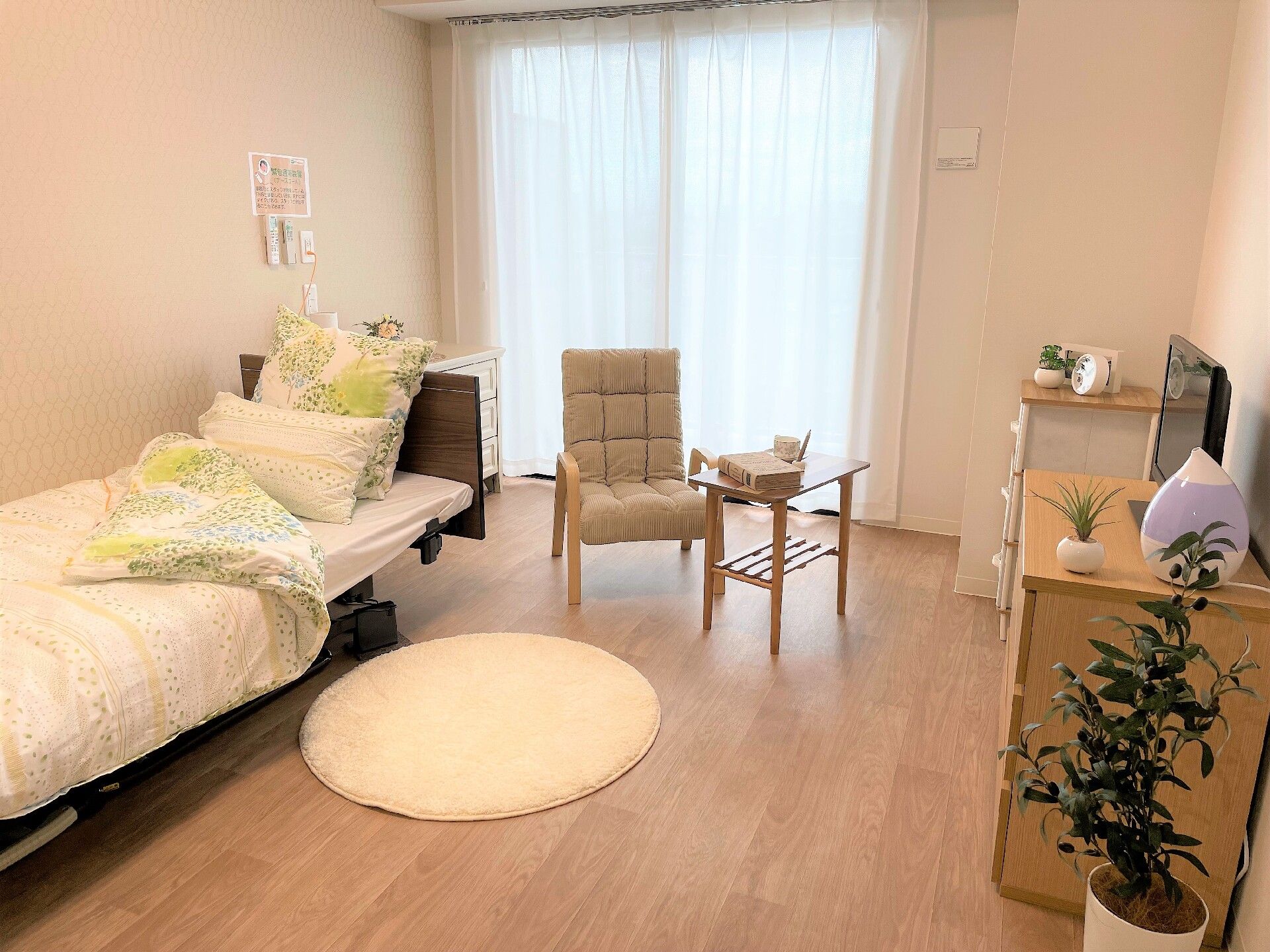 ベッドサイドには緊急通報装置があり、大きな窓が付いているフローリングの部屋にはベッドやタンスもある。