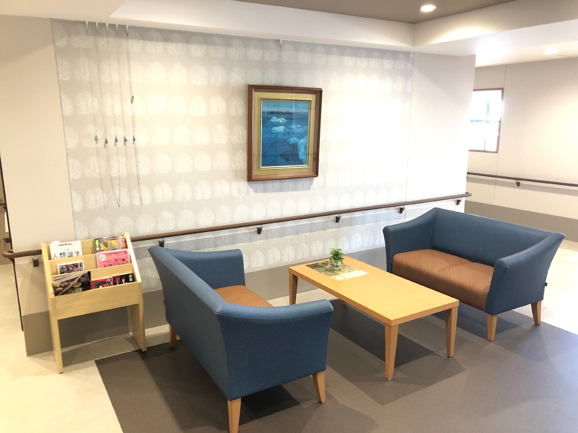 ブルーの椅子の応接セットが置かれた廊下の一角にはブックラックもあり、ブルー系の絵画が飾られている。