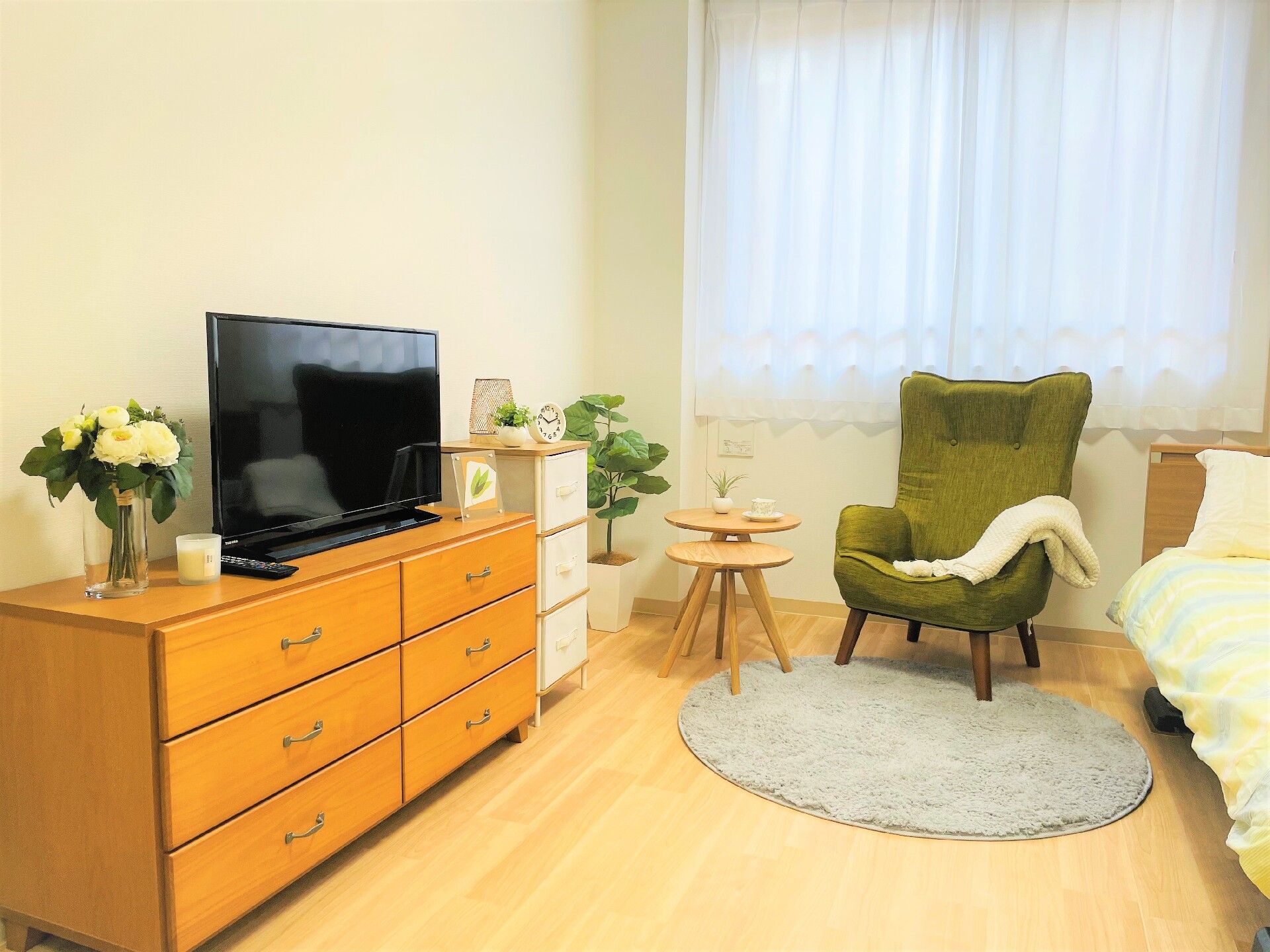 一人用の椅子や寝具付きのベッドが置かれたフローリングの部屋には、タンスやテレビもあり、花が飾られている。