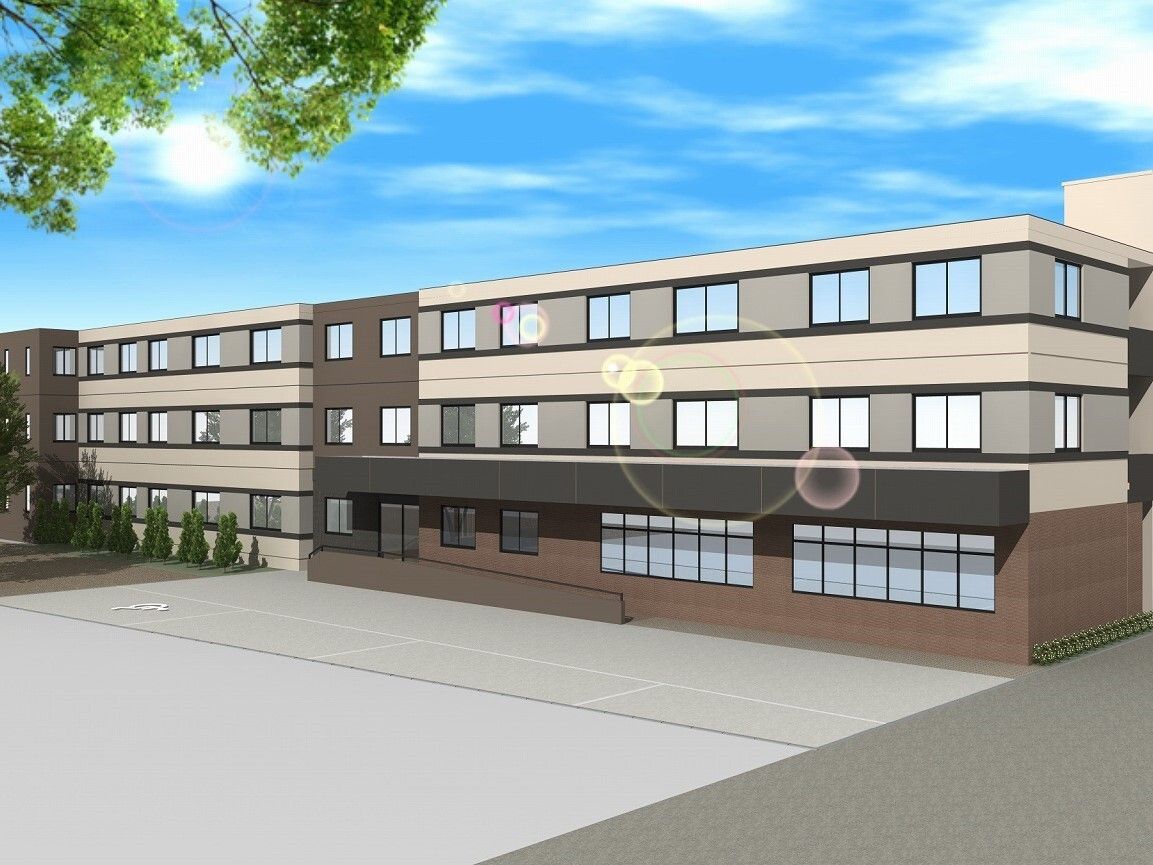 ブラウン系の横に長い３階建ての建物は日当たりのいい場所にあり、建物の周りには草木が植えられている。