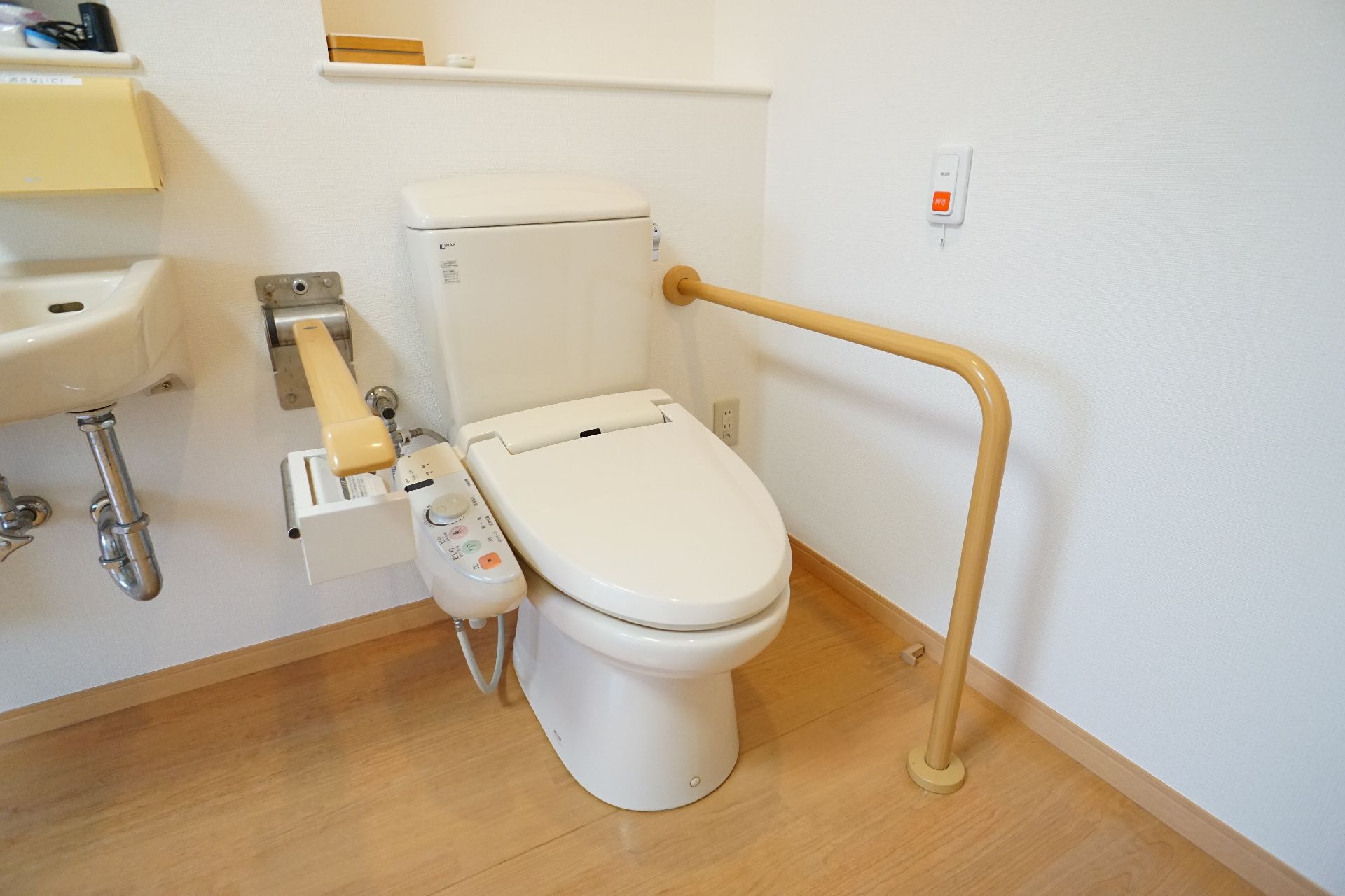 白い壁の部屋の隅に置かれた手すりに囲まれた洋式便器