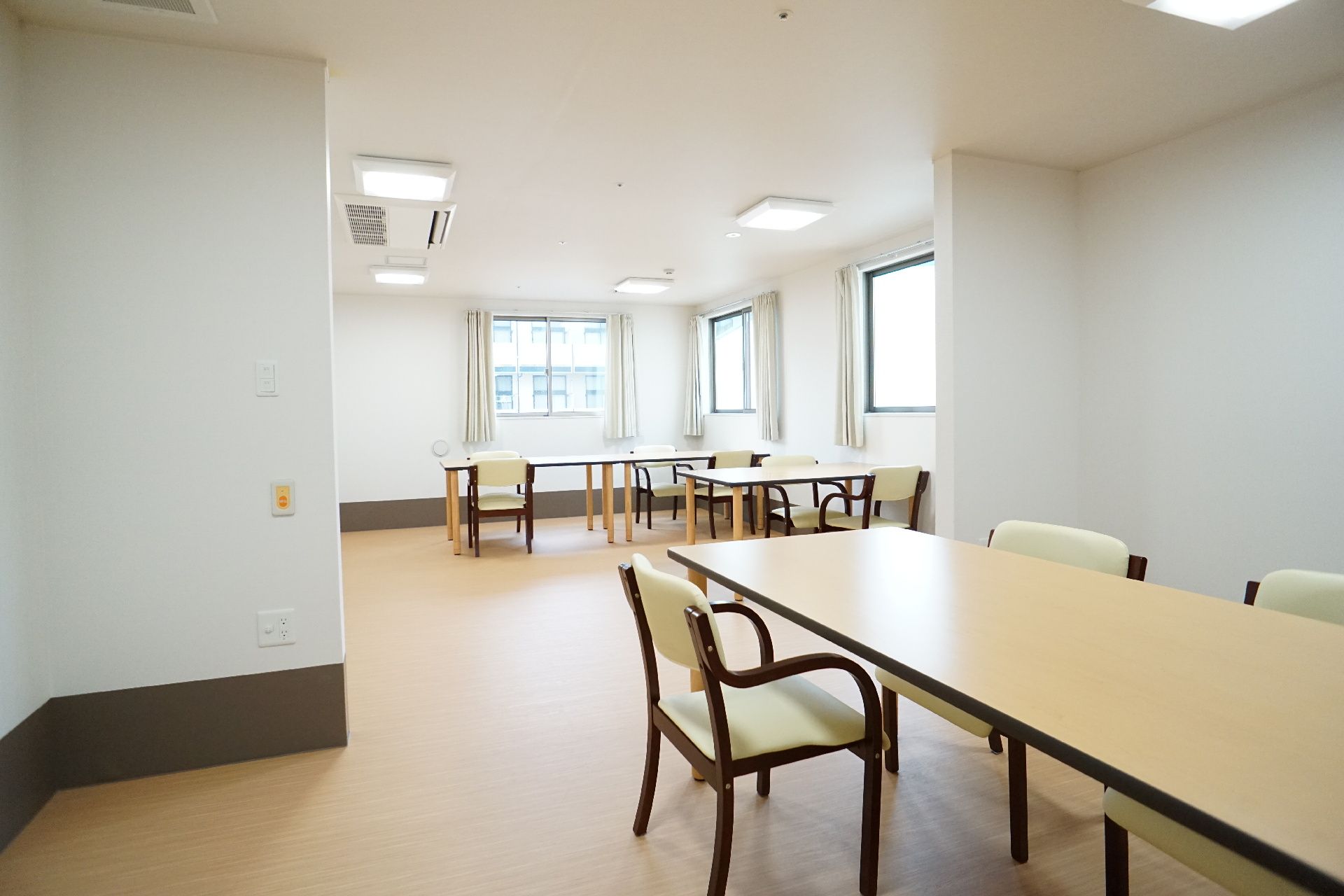 窓がある白い壁の部屋に置かれた木製の机と椅子