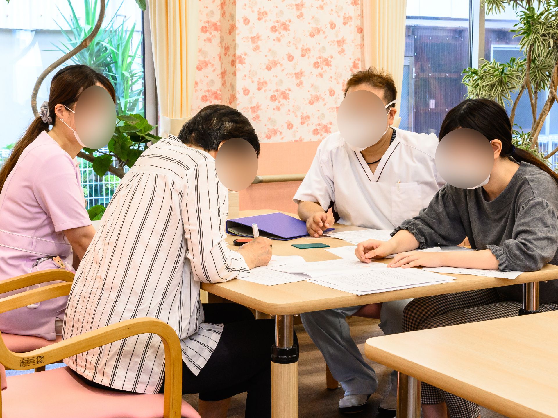 ボーダー柄のエプロンを付けた女性スタッフが白いシャツを着た高齢男性のサポートを笑顔でしている。