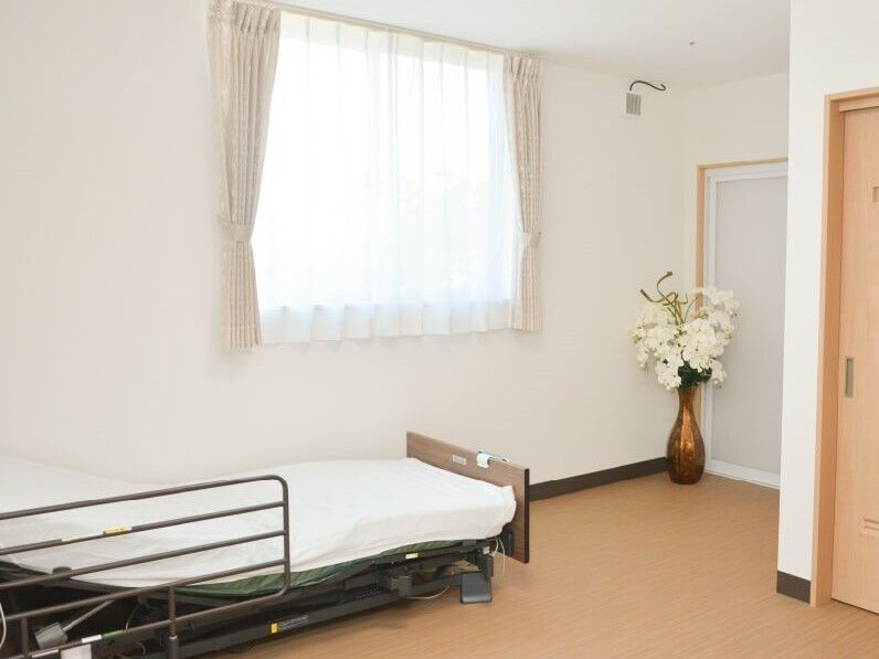 寝具付きのベッドが置かれた部屋には花が飾られ、トイレや浴室のドアが付いている。