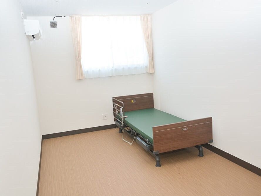 寝具のないベッドが置かれたフローリングの居室にはエアコンが付き、窓もある。