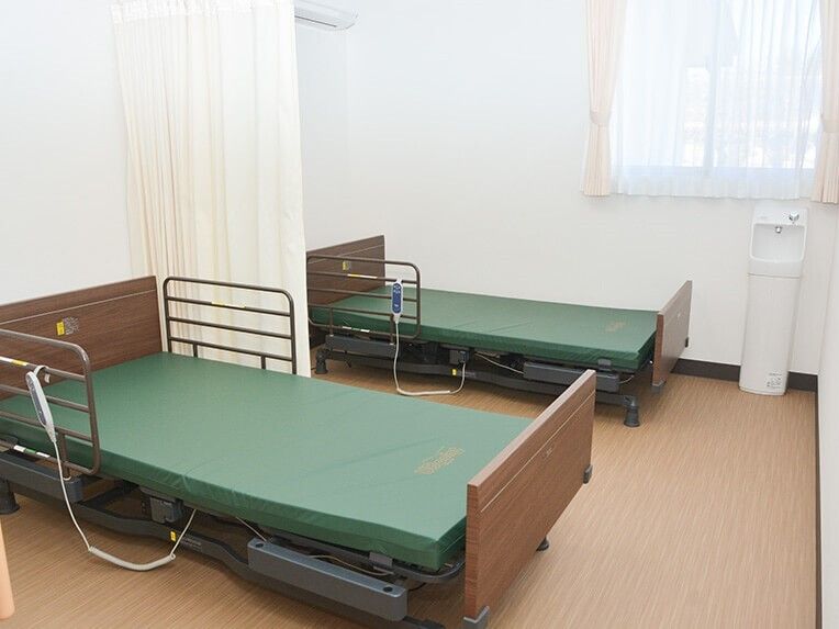 シンプルな手洗い場が付いたフローリングの居室。居室の中央をカーテンで仕切ることができ、ベッドが2台ある。