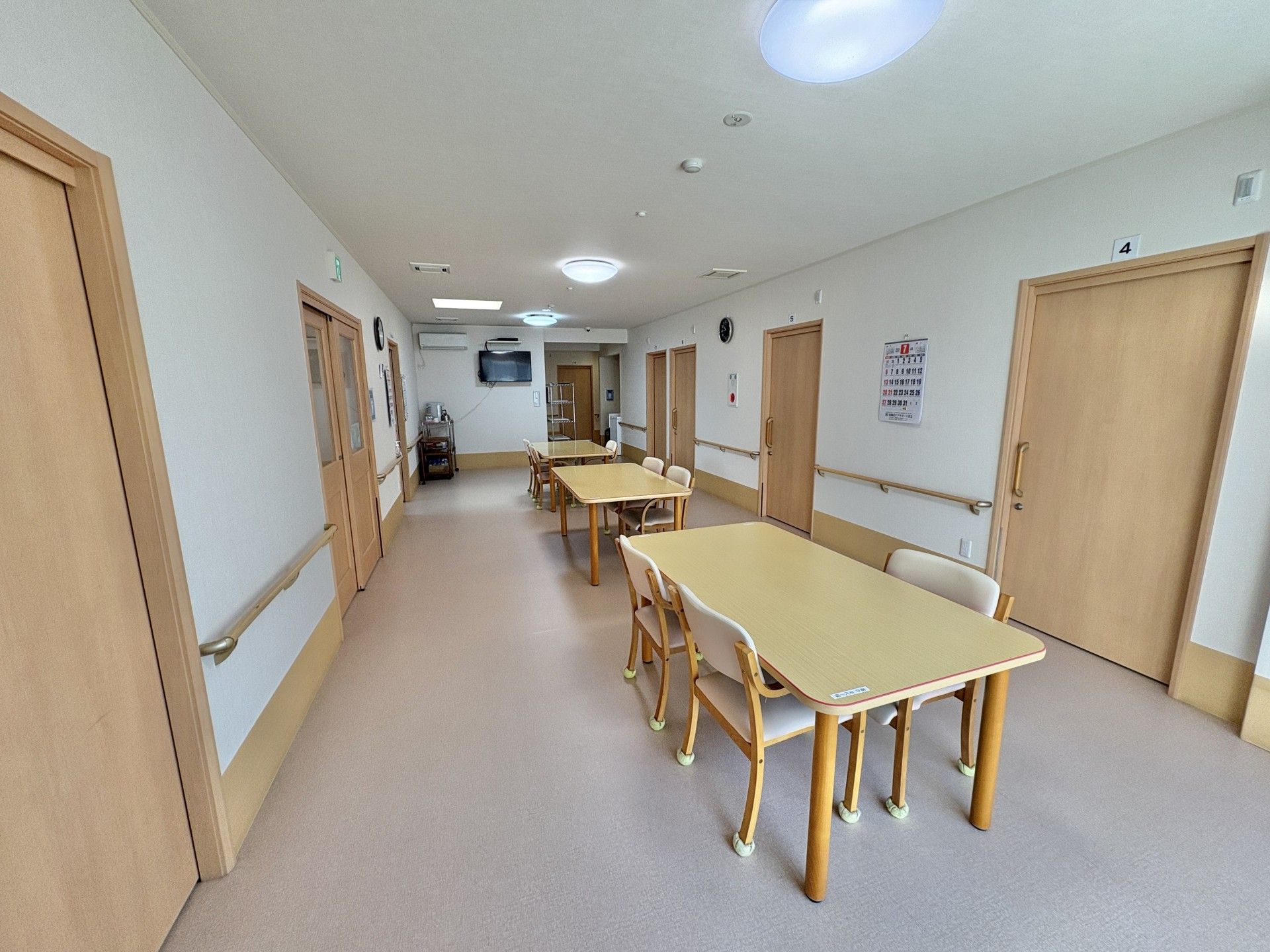 木製のテーブルを囲んで笑顔で話しているピンクのポロシャツを着た女性スタッフと高齢女性。