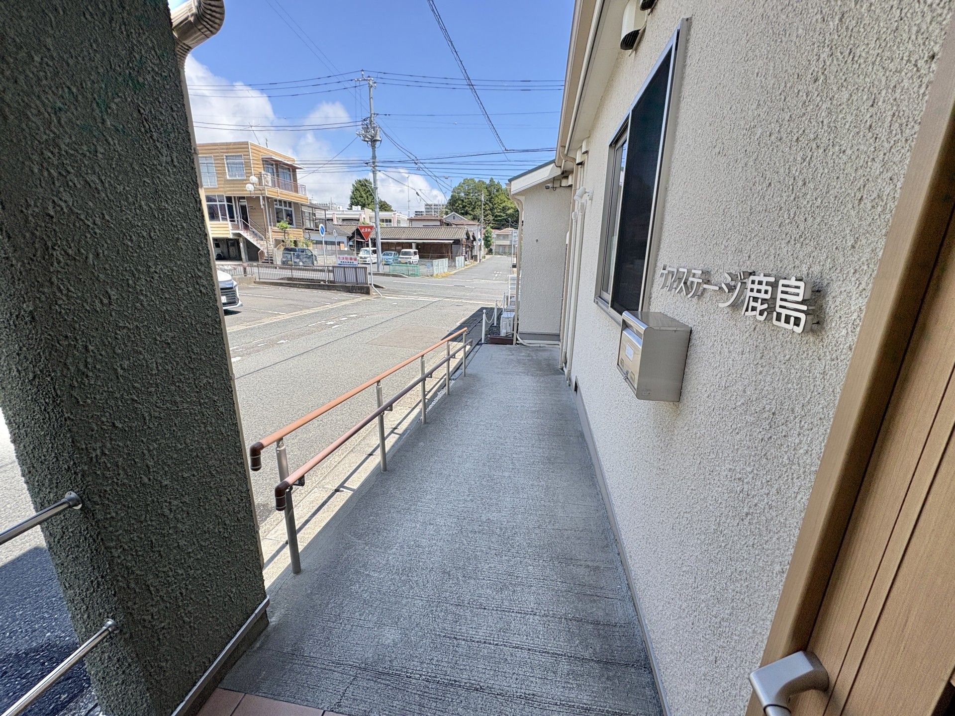 屋外で誰かに手を振っている車いすの高齢女性。ポロシャツを着た男性スタッフが介助をしている。