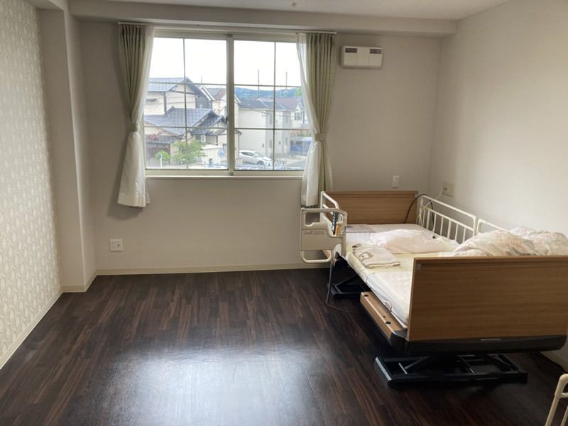寝具付きの介護ベッドが置かれたフローリングの部屋には大きな窓があり、カーテンもある。