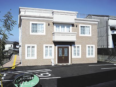 大きな駐車場がある2階建ての建物の玄関には屋根があり、日当たりのいい場所に建っている。