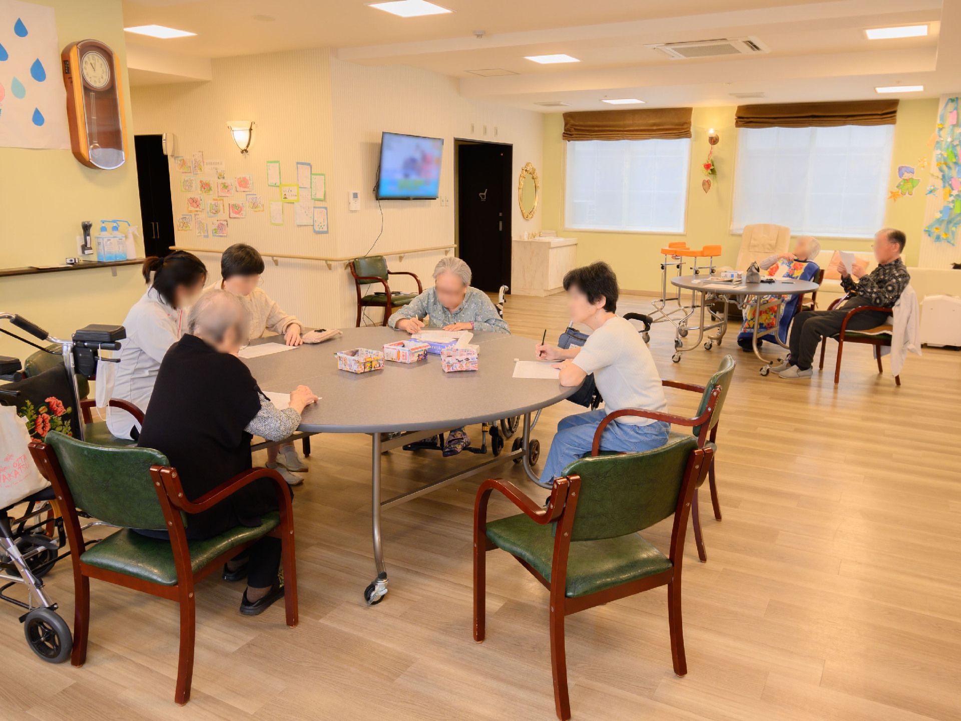 広間に置かれた丸い机の周りの椅子に座る入居者様