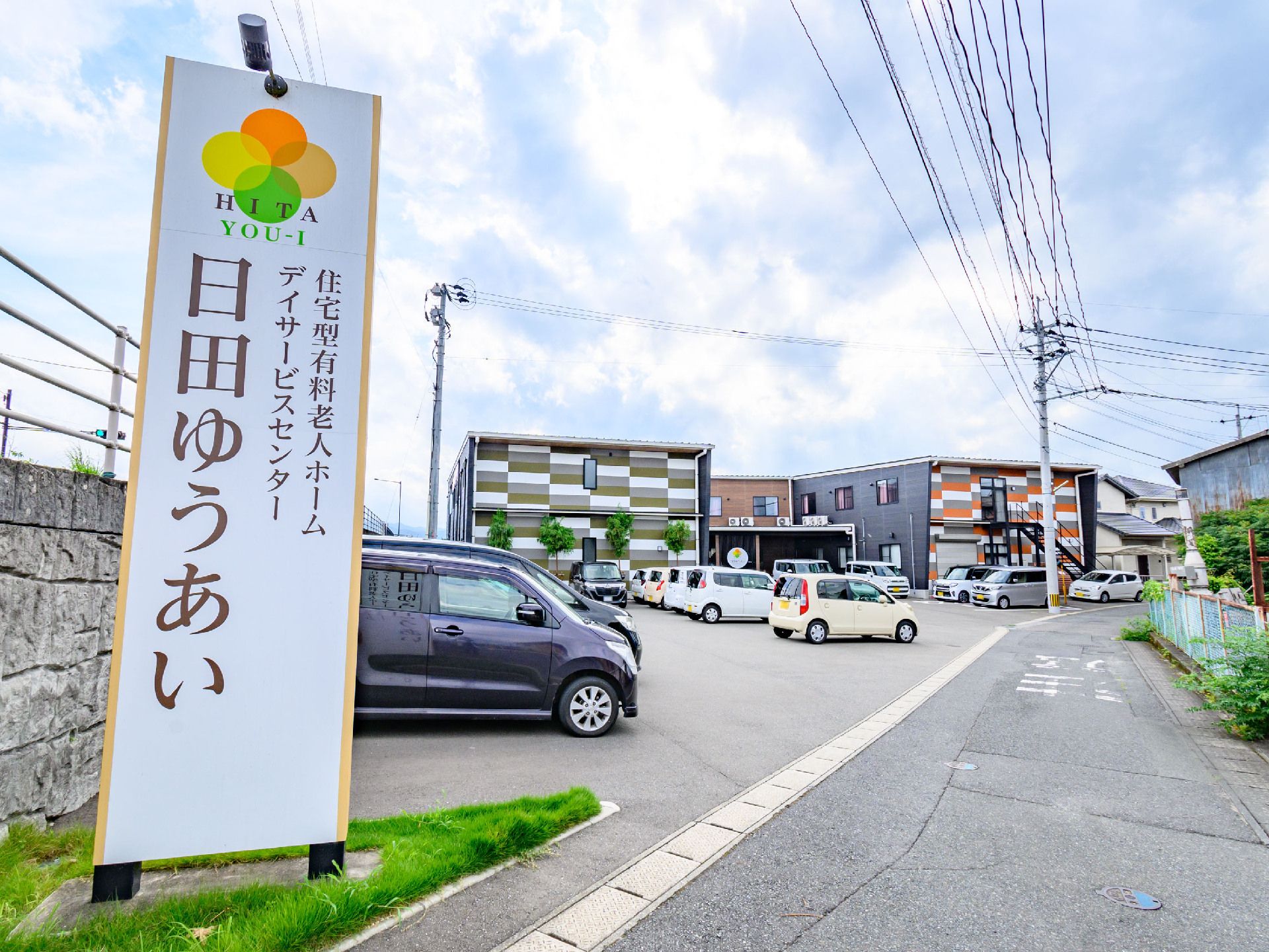 白い看板の奥に立地している複数の車が止まった駐車場に面したチェックの外観の建物
